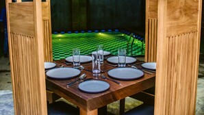 A dining table set for six with wooden chairs, a green checkered floor, and a lantern in the background. - Thambu Illam (Jaffna)