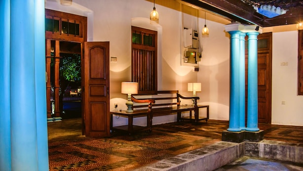 A hotel lobby with a wooden bench, a table with a lamp, and blue columns. - Thambu Illam (Jaffna)