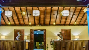 A hotel lobby with wooden paneling, a high ceiling with hanging lights, and two animal statues on cabinets. - Thambu Illam (Jaffna)