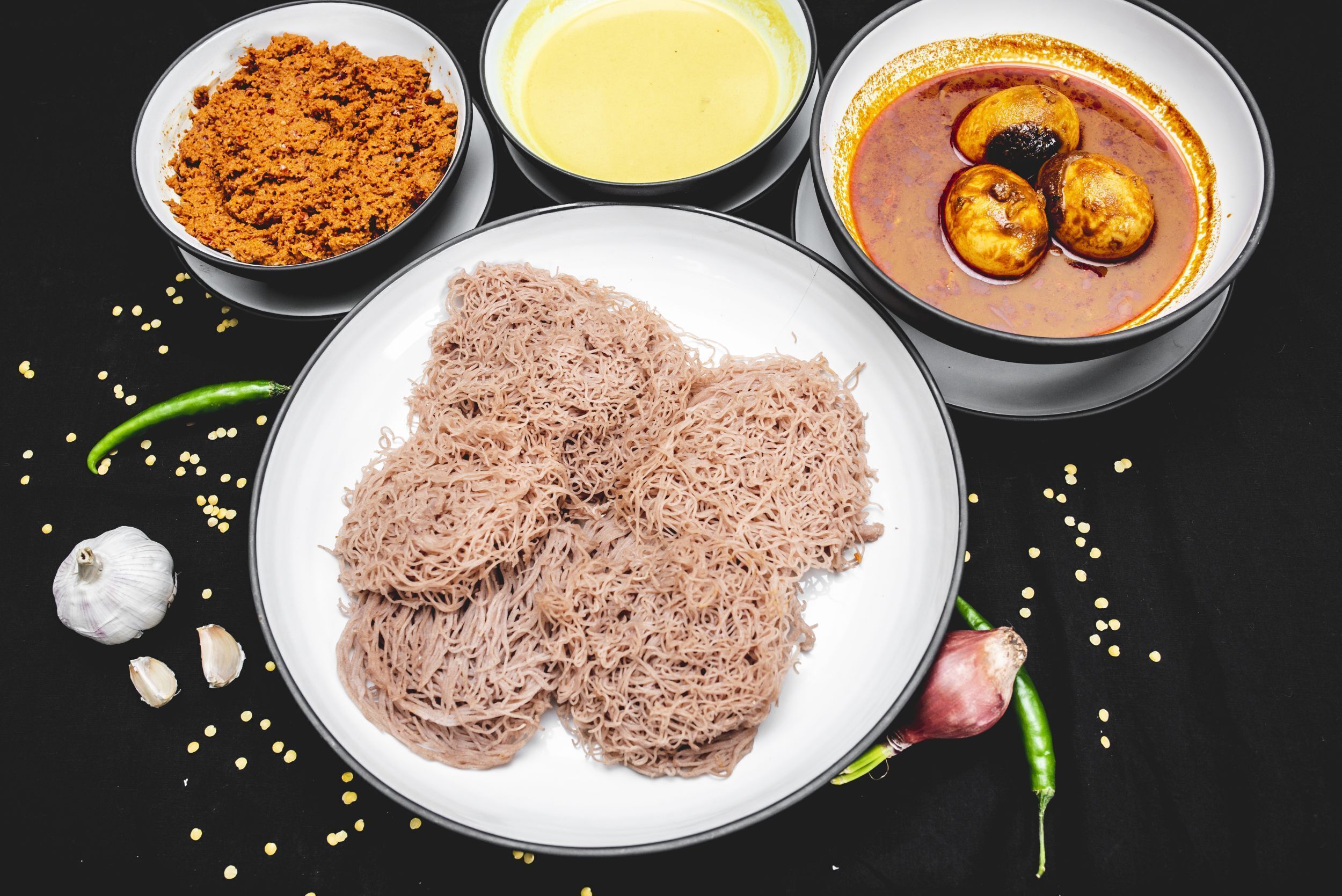 A plate of noodles, a bowl of curry, a bowl of spices, and a bowl of sauce.