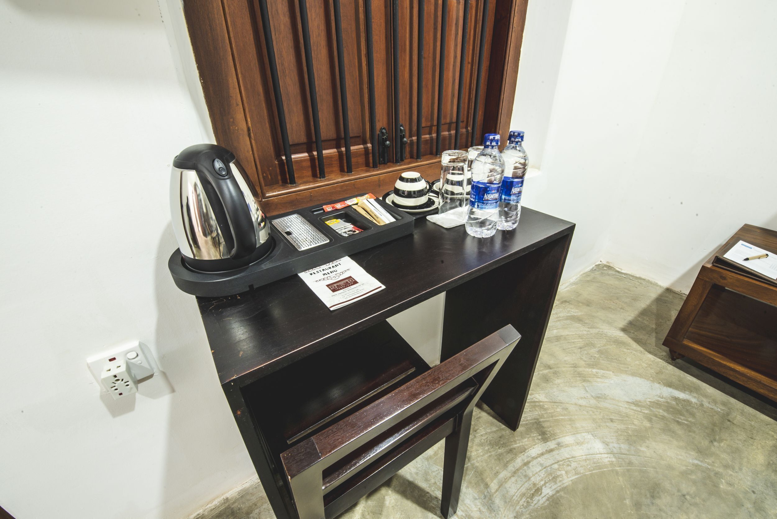 A small wooden desk with a kettle, a tray with various items, and bottles of water.