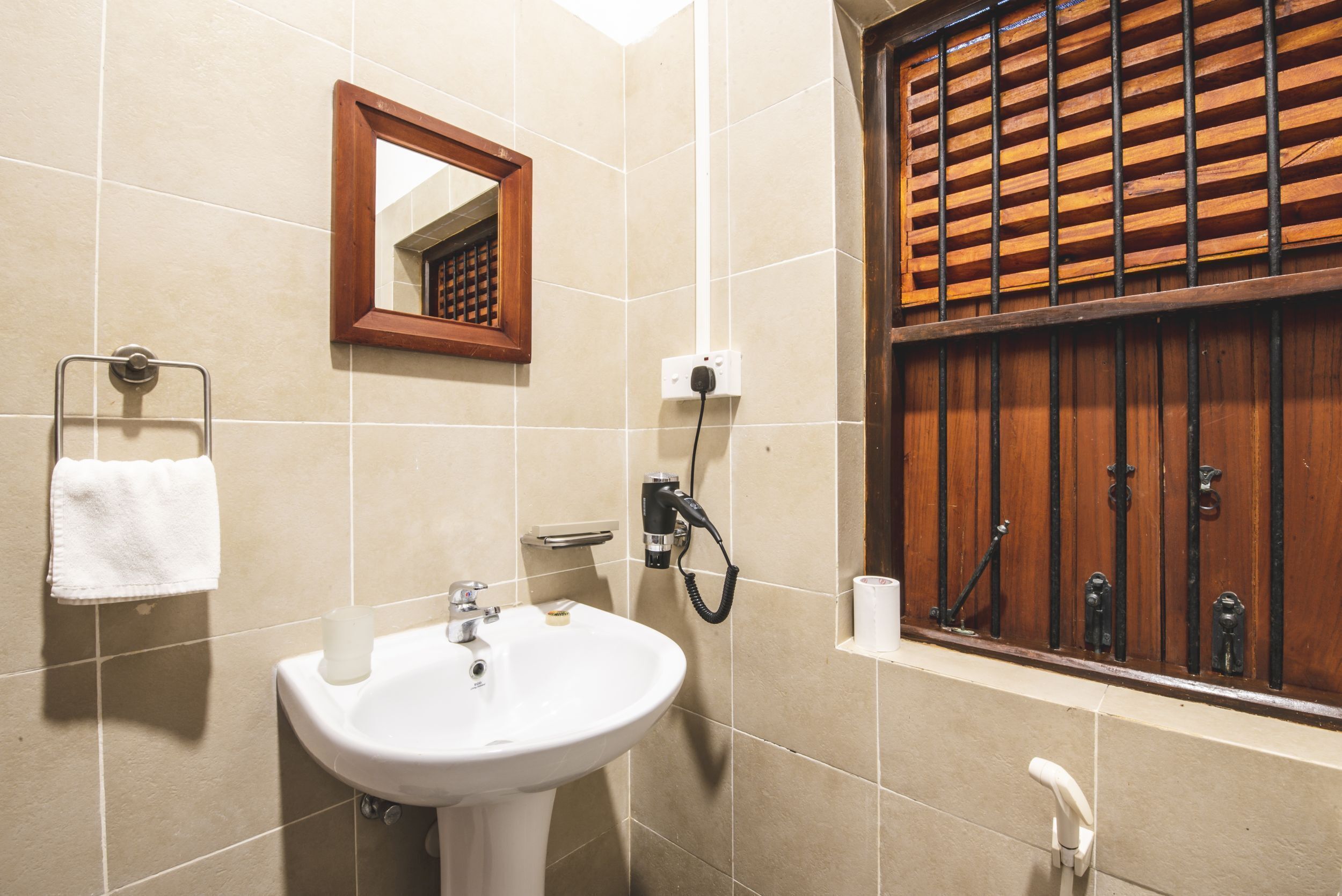 Ein Badezimmer mit Waschbecken, Spiegel, Handtuchhalter und einem Fenster mit Holzjalousien.