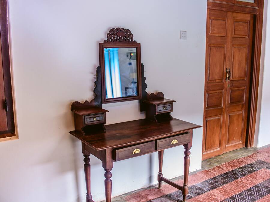 A wooden desk with two drawers and a mirror, positioned against a white wall with a wooden door in the background.
