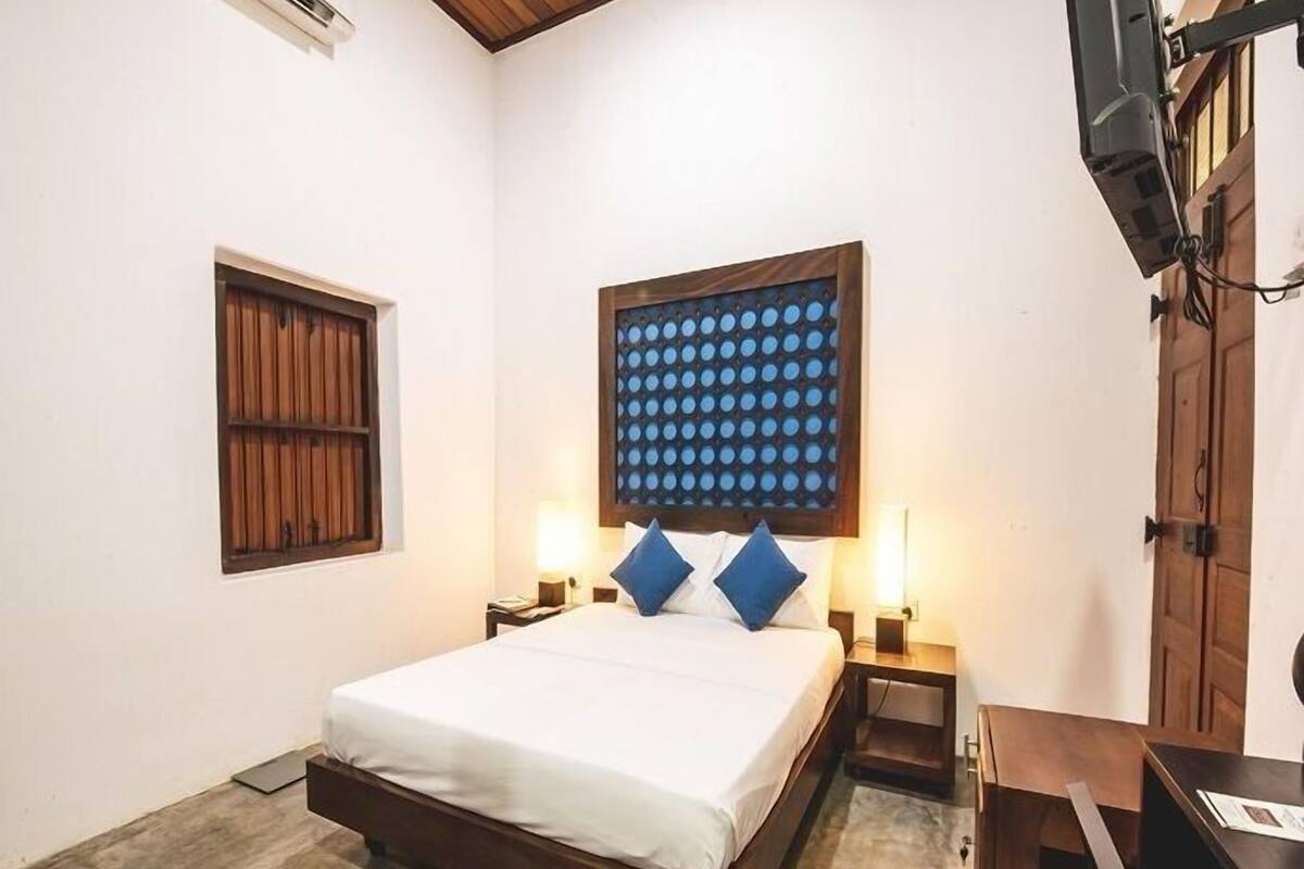 Un dormitorio con una cama, dos mesitas de noche, un cabecero de madera, una ventana y un televisor.
