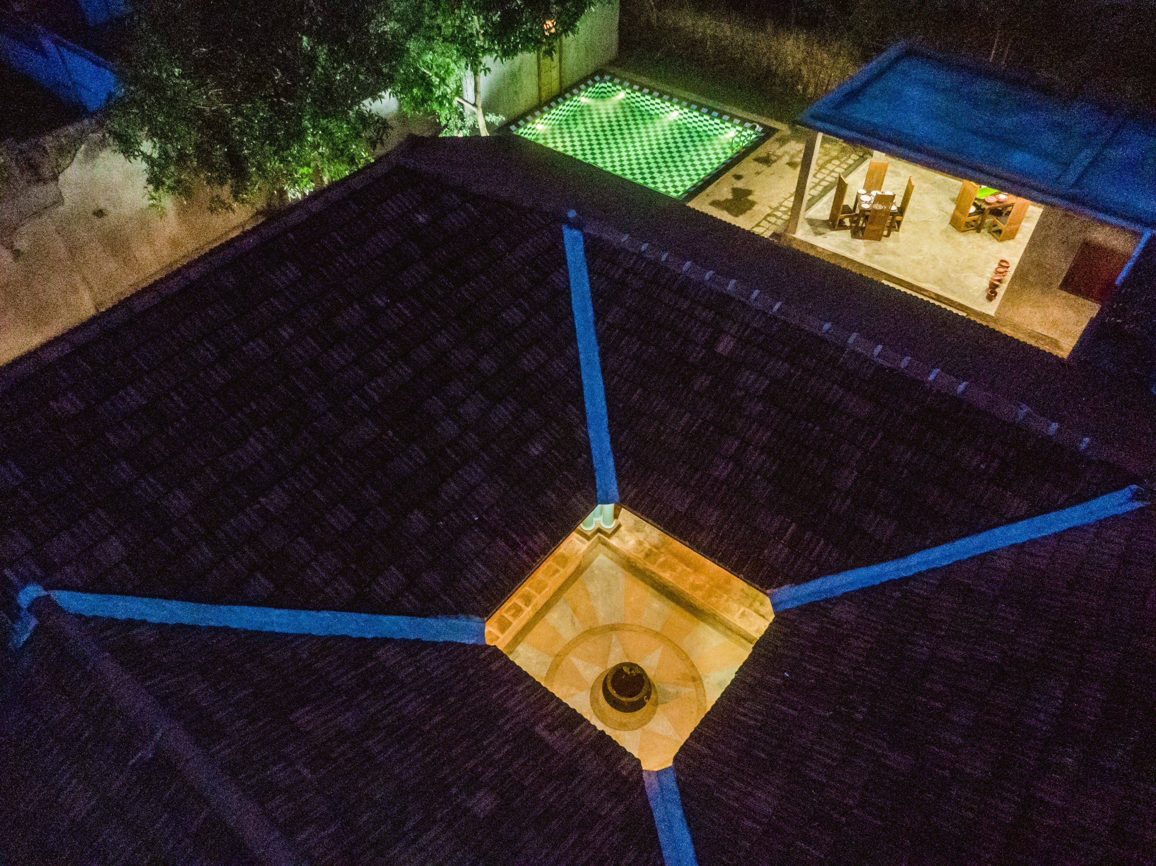 Une terrasse sur le toit dotée d’une lucarne centrale, d’une zone à motifs en damier et d’un petit bâtiment abritant des tables et des chaises.