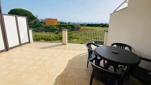 A balcony with a tiled floor, a table with chairs, and a view of greenery and buildings in the distance. - B&B Caravello (Milazzo)