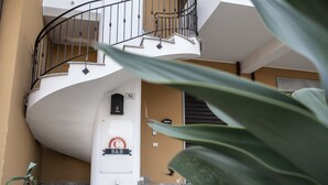 A spiral staircase with a black railing, a sign with 'C' and 'B&B', and a potted plant in the foreground. - B&B Caravello (Milazzo)
