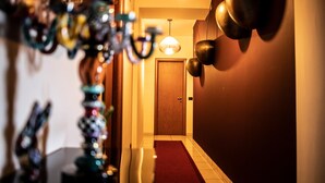 A hallway with a wooden door at the end, a red carpet, and decorative wall sconces. - B&B Caravello (Milazzo)