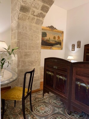 A room with a stone wall, a round table with a chair, a wooden cabinet, and a painting on the wall. - Masseria Chiusurella (Corato)