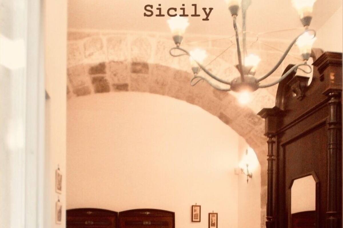 A room with a large arched doorway, a wooden cabinet, a small table with a lamp, and patterned floor tiles.