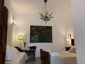 A hotel room with a bed, a desk with a chair, a hanging plant, and a painting on the wall. - Masseria Chiusurella (Corato)