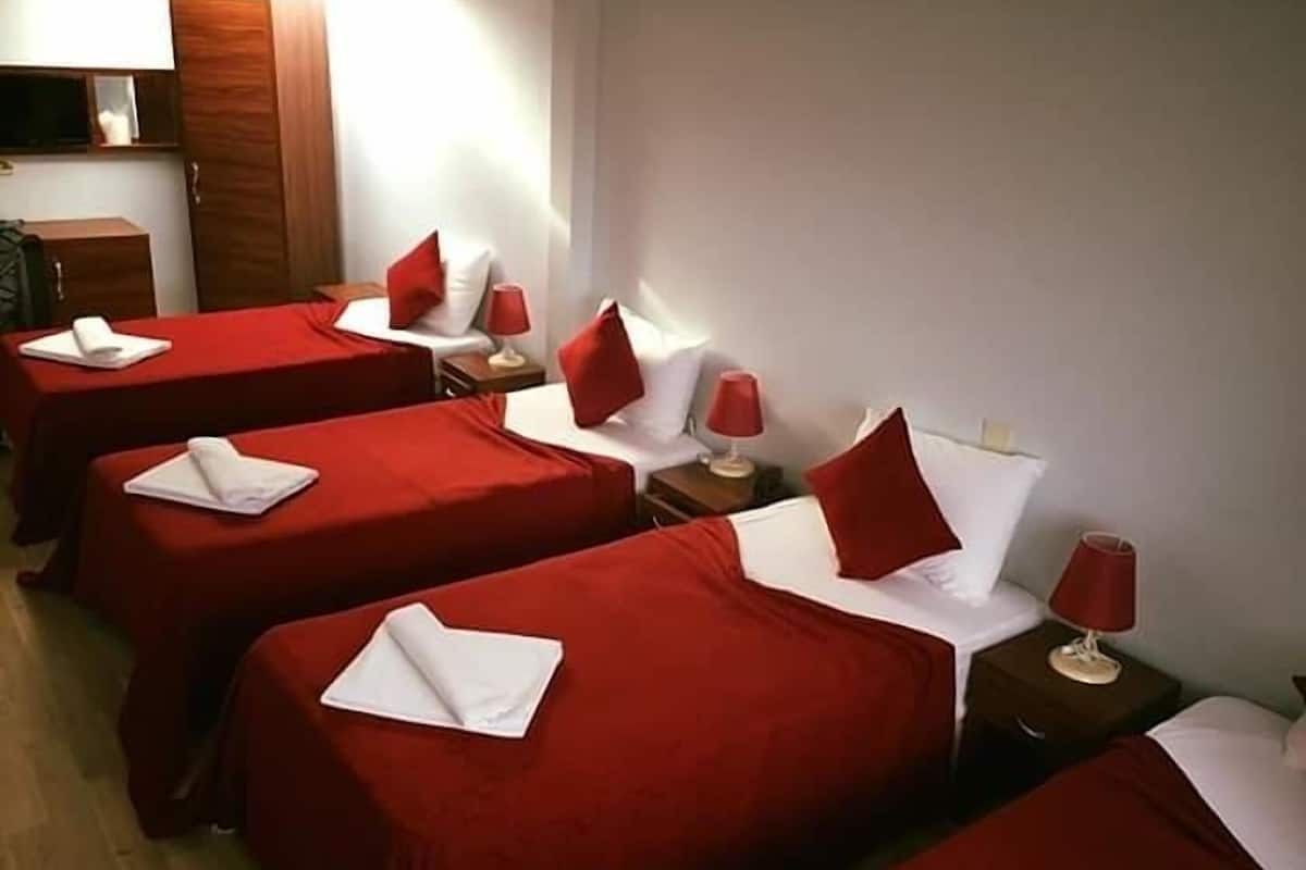 A hotel room with four beds, each with red bedding and white pillows, and red lamps on wooden nightstands.