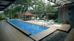 A swimming pool with a tiled deck, surrounded by lounge chairs and a small gazebo. - Villa Alifa (Pakem)