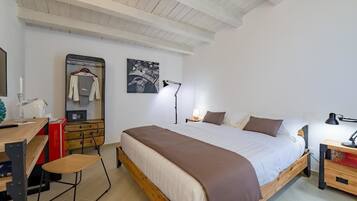A bedroom with a wooden bed, a desk with a chair, a dresser, and a wall-mounted lamp.