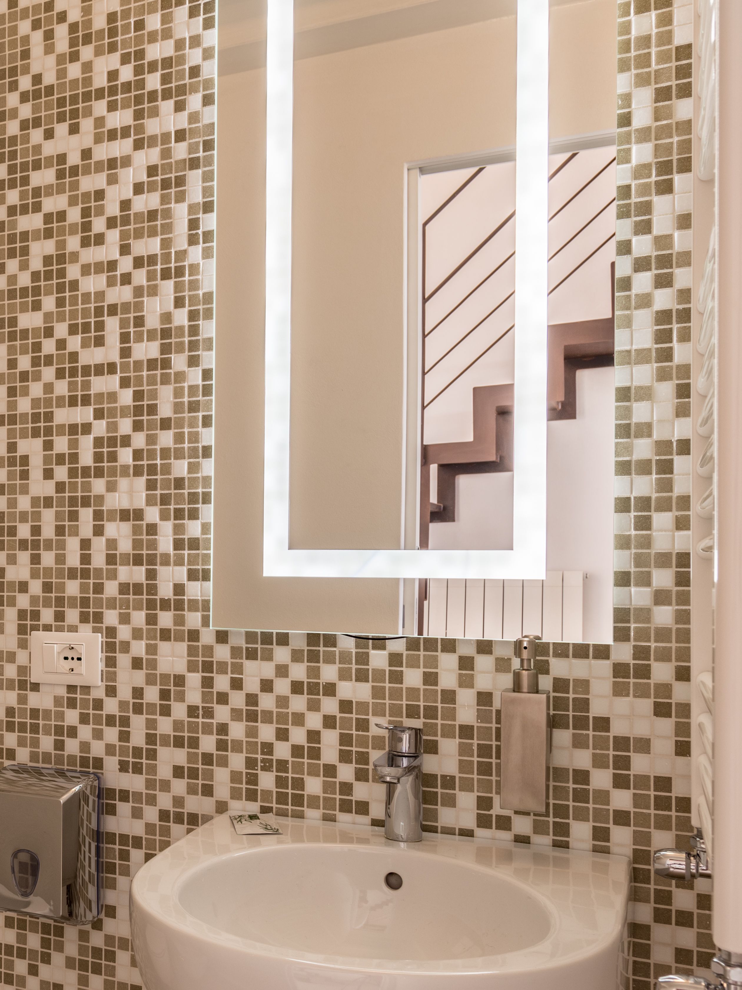 Un baño con salpicadero de azulejos, un lavabo, un espejo y un perchero para toallas.