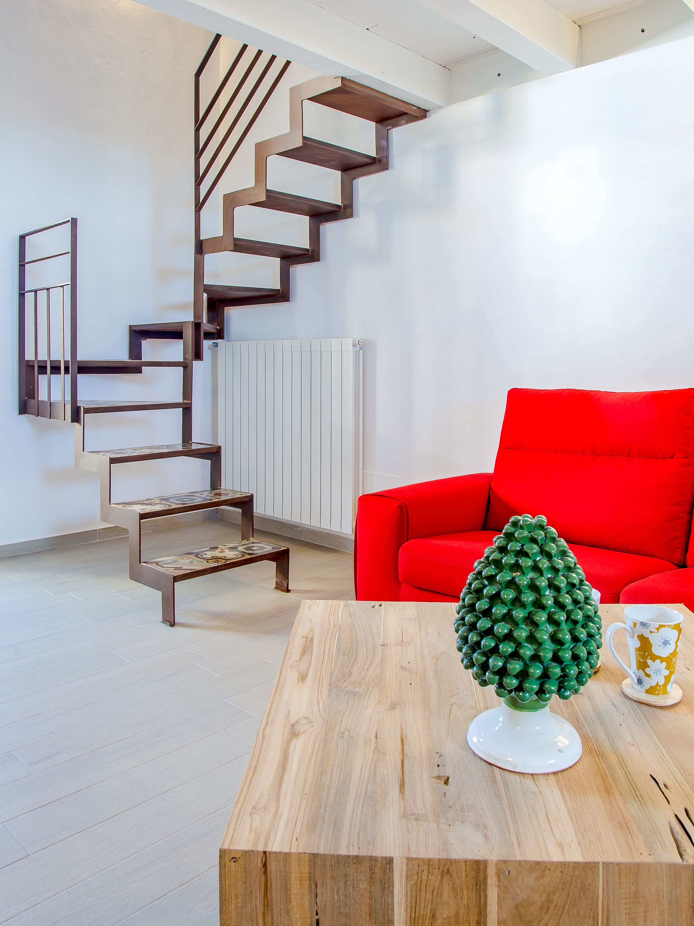 A modern living room with a wooden coffee table, a red sofa, a unique green decorative object, and a spiral staircase against the wall.