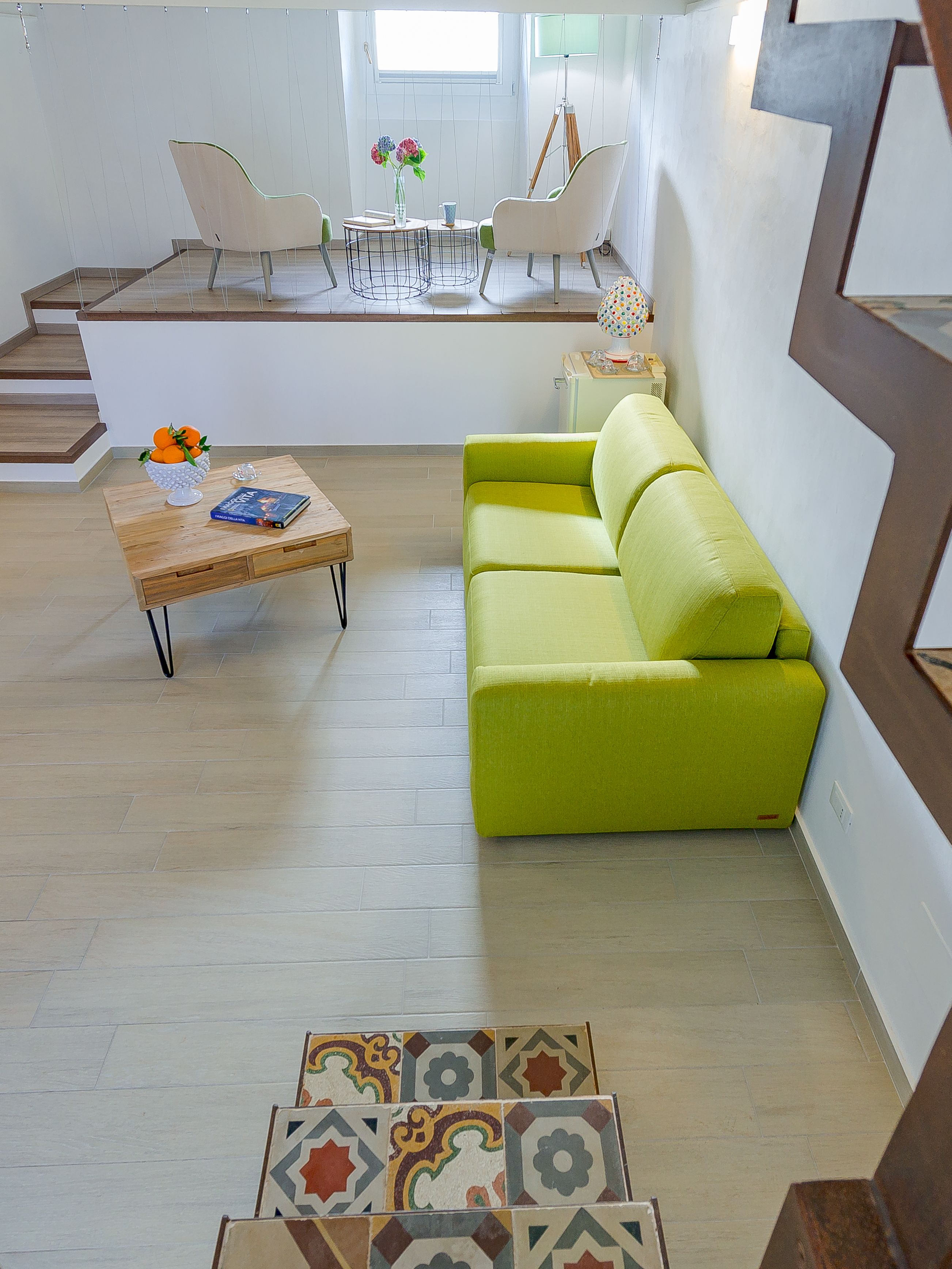 Un salon moderne avec un canapé vert, une table basse en bois et une petite table d’appoint. Un escalier mène à un niveau supérieur.