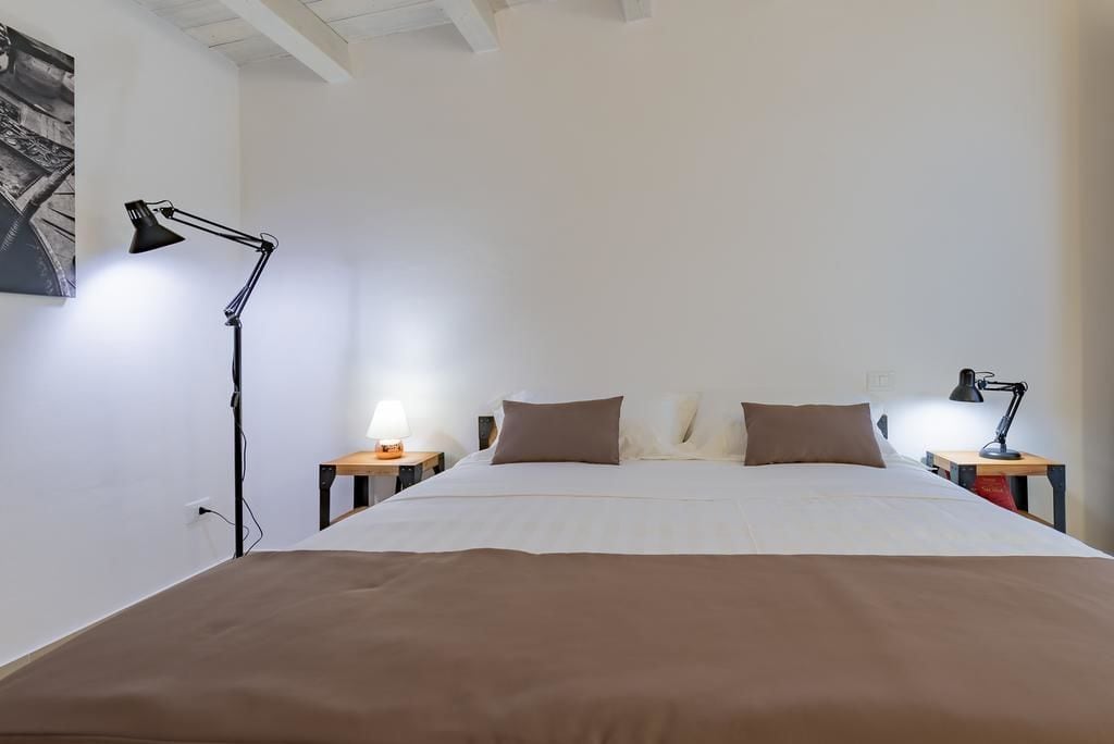 A bedroom with a large bed, two bedside tables with lamps, a wall-mounted picture, and a white ceiling.