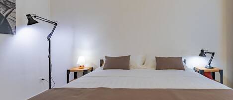 A bedroom with a large bed, two bedside tables with lamps, a wall-mounted picture, and a white ceiling.