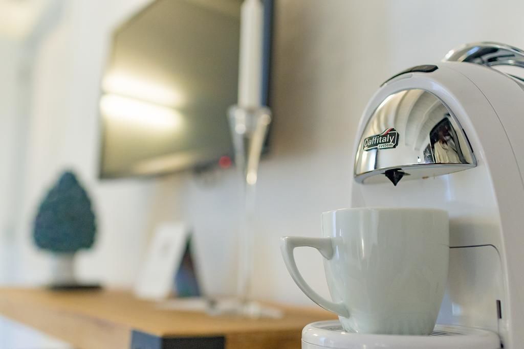 A coffee machine with a cup placed underneath it, a small plant, and a mirror on the wall.