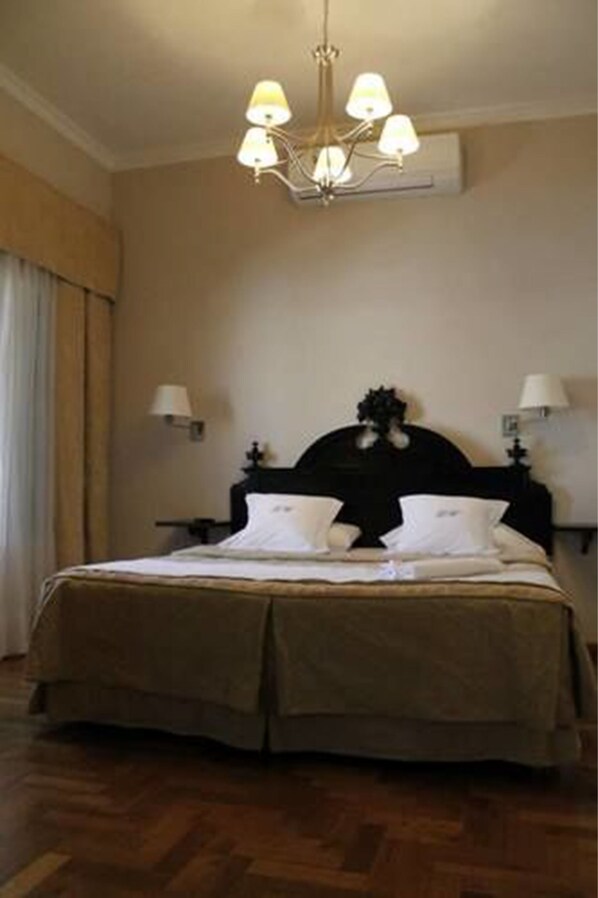 Quarto de hotel com uma cama grande, um candelabro e duas luminárias de cabeceira.