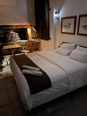 Quarto de hotel com cama, uma cadeira de madeira, uma mesa pequena e lareira.