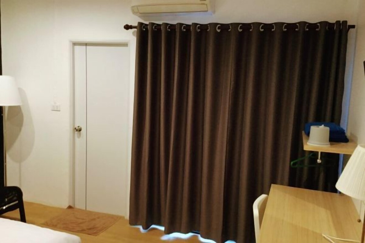 A room with a bed, a desk, a chair, a lamp, and a curtain.