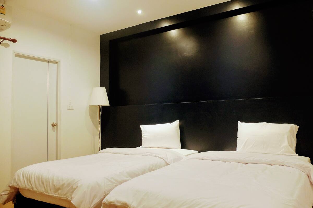 A hotel room with two beds, a black headboard, a white door, and a bedside lamp.