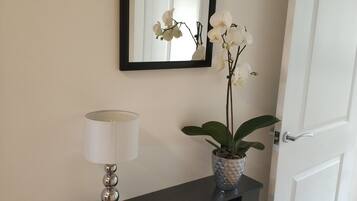 A hallway with a dark-colored console table, a white lamp, a potted plant, and a mirror on the wall.