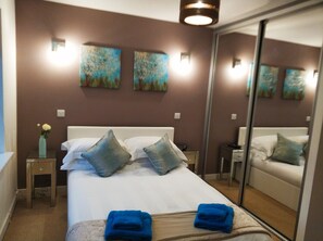 Habitación de hotel con una cama grande, dos mesitas de noche, un espejo y obras de arte en la pared.