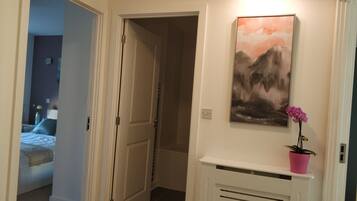A hallway with a door leading to a bedroom, a mounted artwork, and a potted plant.