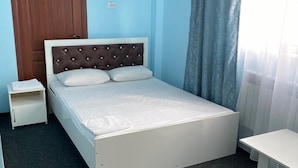 A single-bed room with a wooden wardrobe, a bedside table, and a window with curtains. - Pana Inn (Almaty)