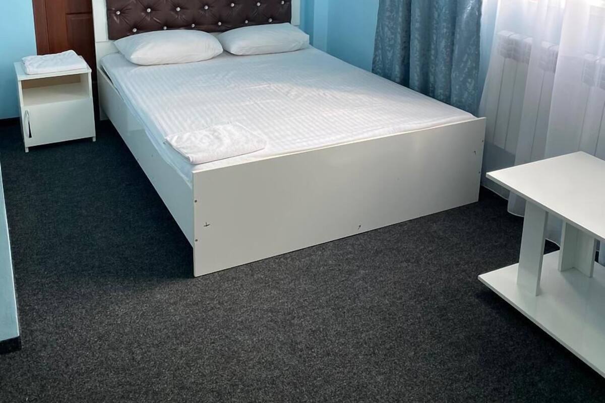 Habitación individual con una cama, un armario de madera, una mesita de noche y una ventana con cortinas.