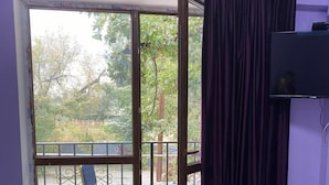 A room with a sliding glass door leading to a balcony, a blue chair, and a TV on the wall. - Pana Inn (Almaty)