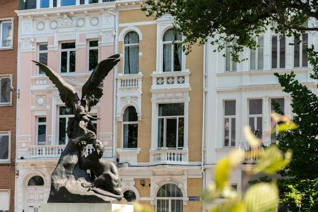 Une statue d’un ange aux ailes déployées, placée devant un bâtiment doté de nombreuses fenêtres et de balcons.