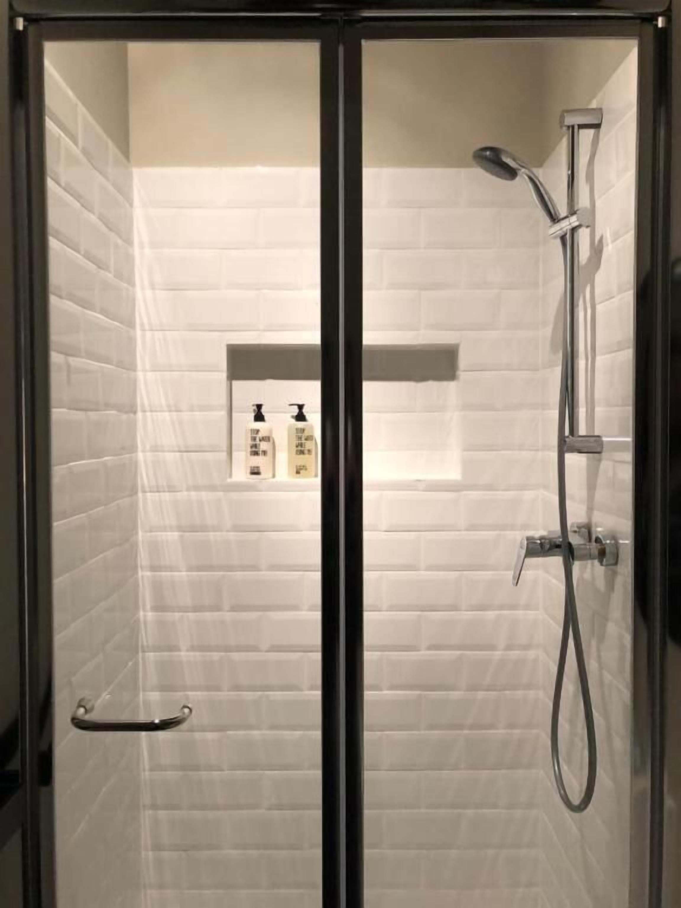 A glass-enclosed shower with a handheld showerhead and a wall-mounted faucet.