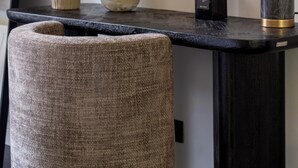 A black console table with a vase of green flowers, a marble vase, and a black diffuser.
