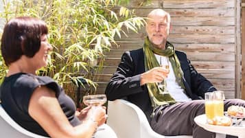 Dos personas sentadas en una mesa al aire libre, con bebidas y pasteles, rodeadas de plantas de bambú y una cerca de madera.