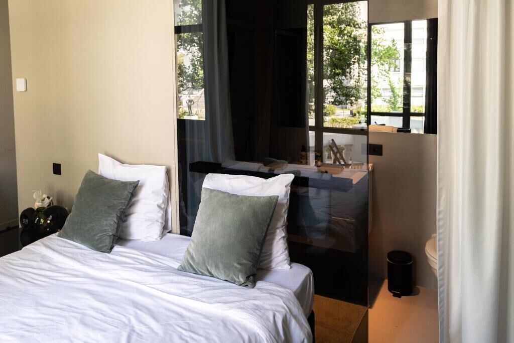 Ein Schlafzimmer mit Bett, Kissen, einem Nachttisch und einem Fenster mit Blick ins Freie.