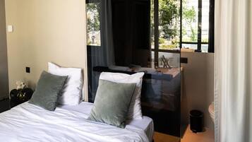 Ein Schlafzimmer mit Bett, Kissen, einem Nachttisch und einem Fenster mit Blick ins Freie.