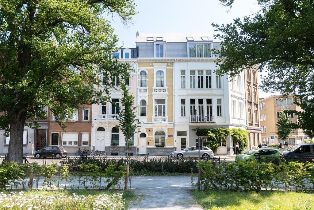 Une rangée d’immeubles résidentiels à plusieurs étages, dotés de balcons, avec une allée pavée et des voitures garées.