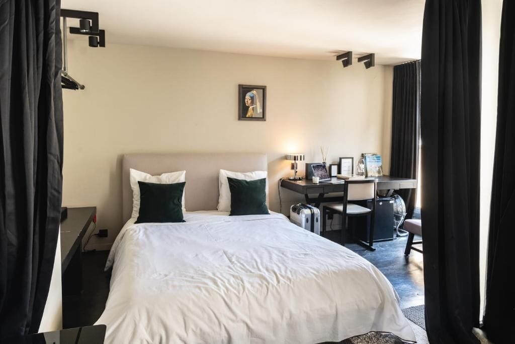 A hotel room with a bed, desk, chair, and a picture on the wall.