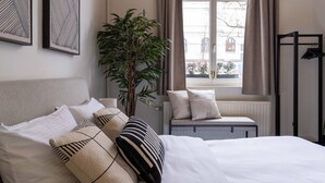 A neatly arranged bedroom with a bed, pillows, a radiator, a window with curtains, and a plant.
