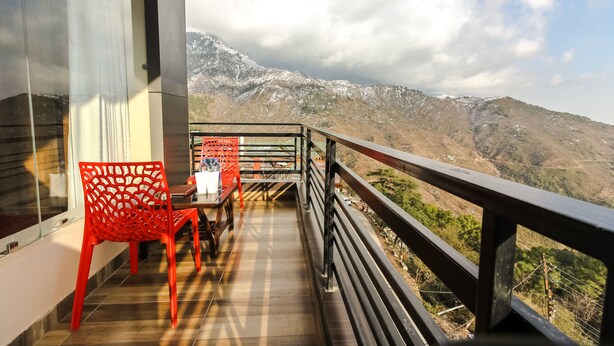 Un balcón con vista a montañas nevadas, una silla roja y una mesa con un cartel.