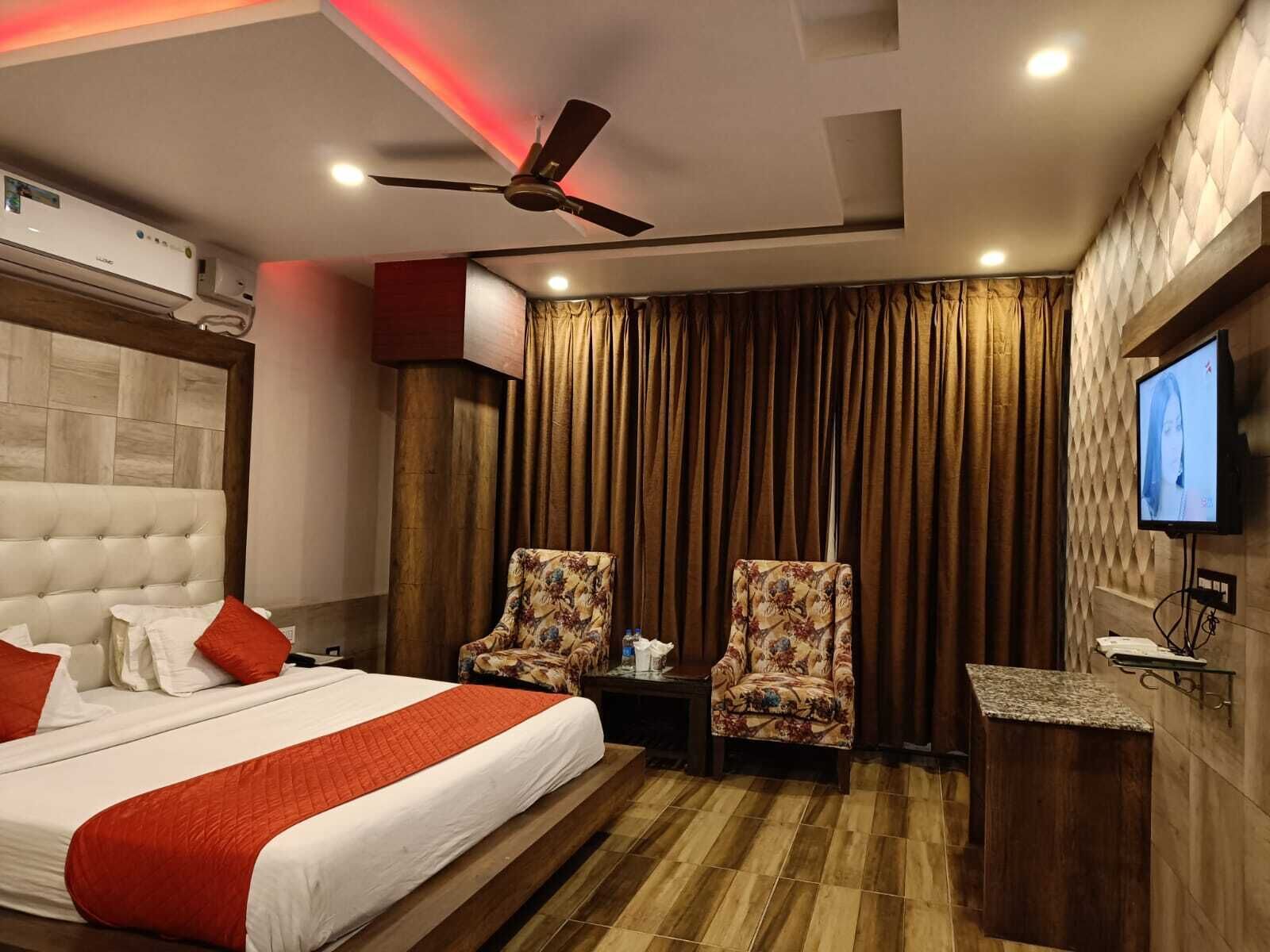 A hotel room with a large bed, two armchairs, a TV on the wall, and a ceiling fan.