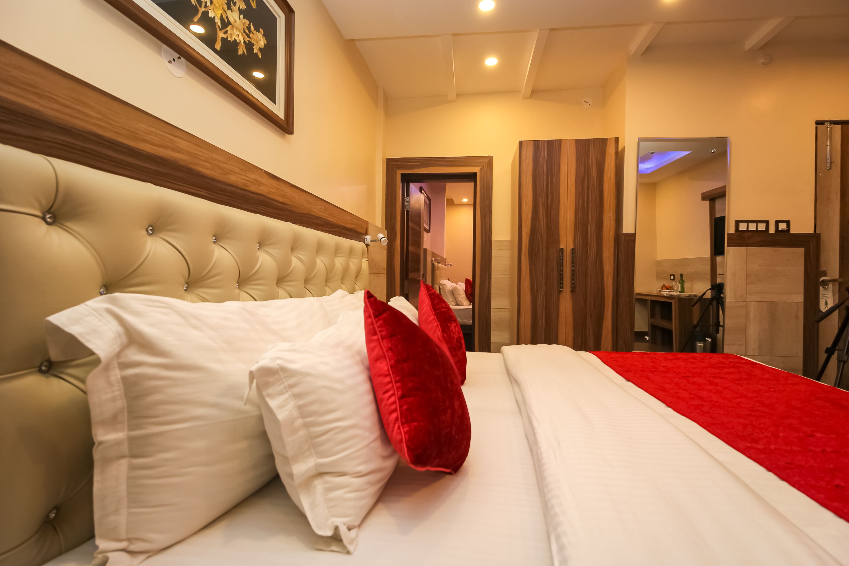 A bedroom with a tufted headboard, a red throw blanket, and a white bedspread.