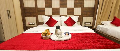 A hotel room with two beds, a red blanket, a basket of fruit, a coffee pot, and a tray with a cup and saucer.