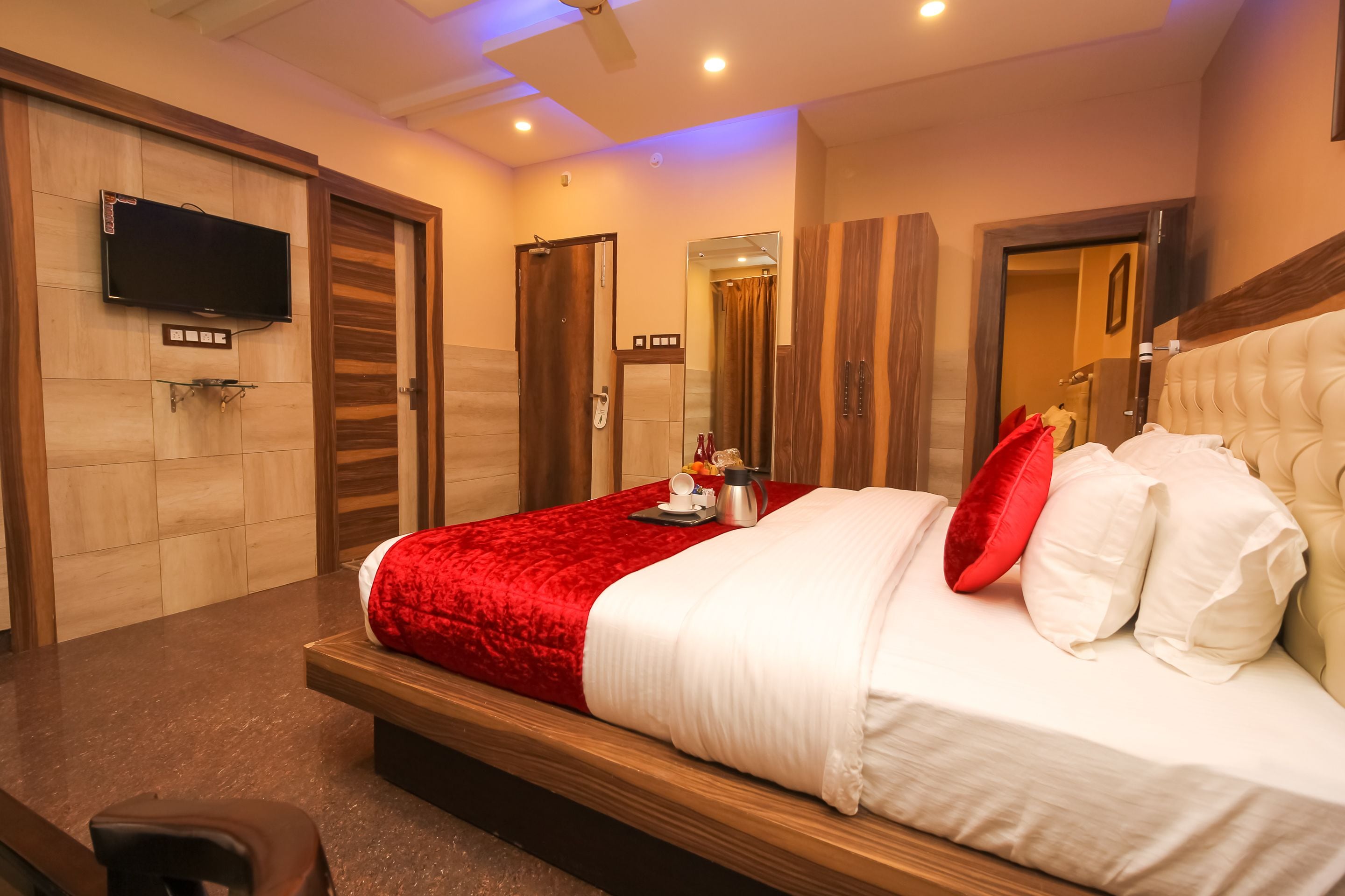 A modern hotel room with a large bed, a flat-screen TV mounted on the wall, and a wooden floor.