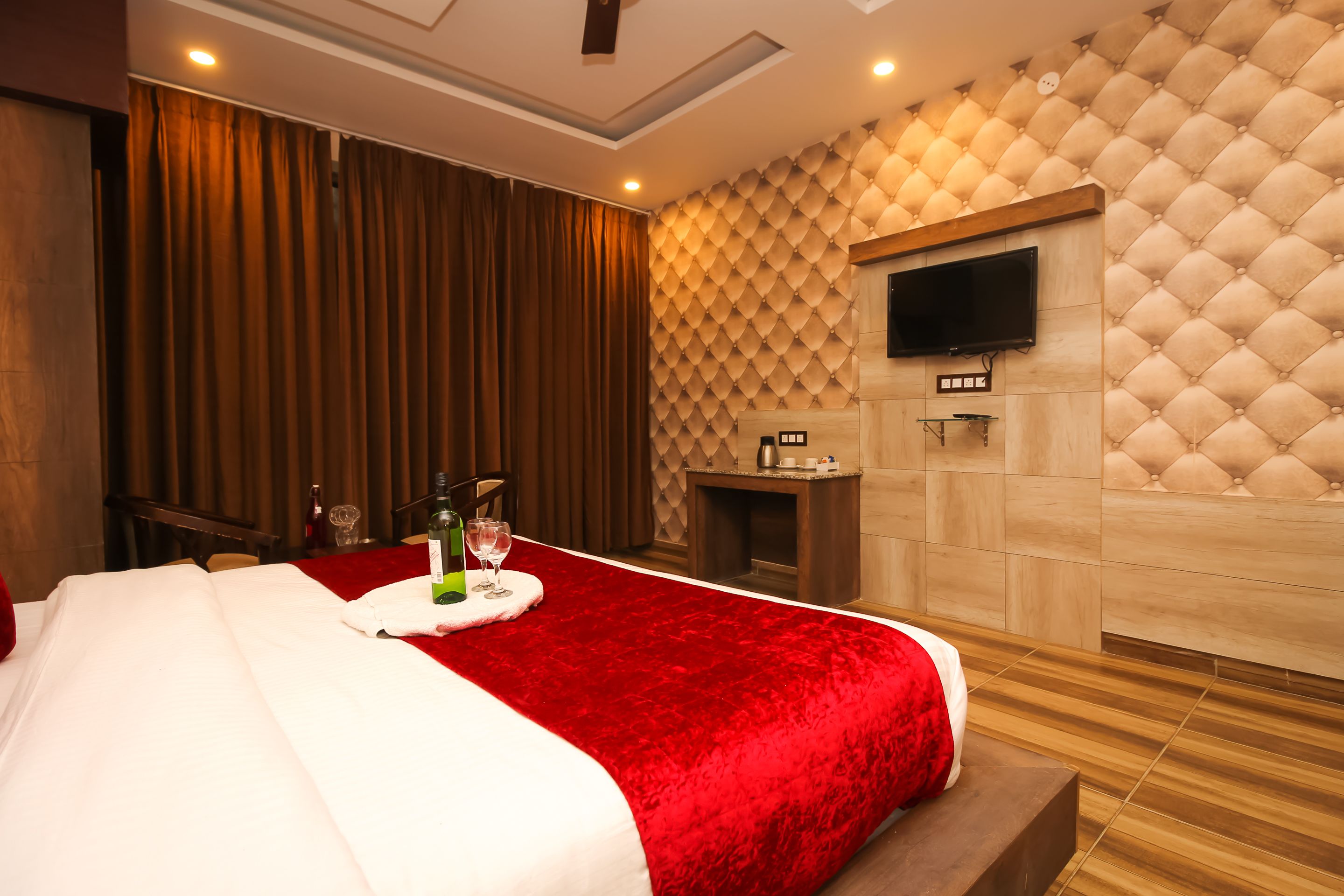 Habitación de hotel con una cama grande, un televisor de pantalla plana en la pared, una mesita con una copa de vino y una chimenea.
