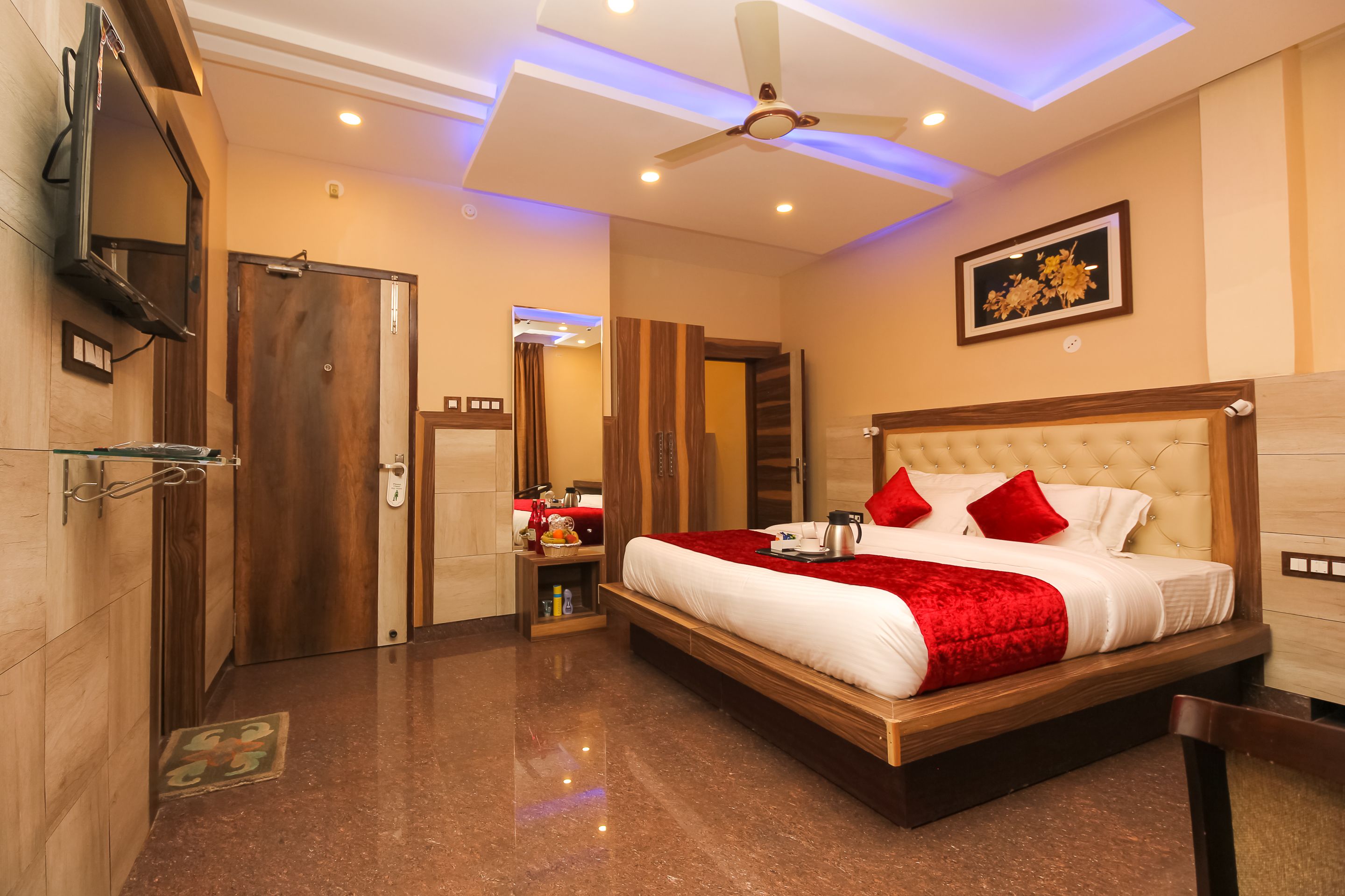 A hotel room with a large bed, a ceiling fan, a TV, and a wooden wardrobe.